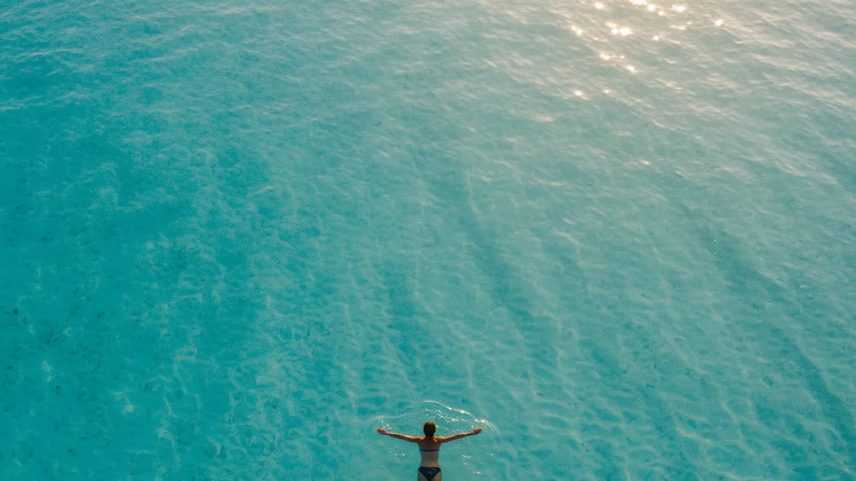Swimmer floating on their back in clear turquoise shallows, photographed from above